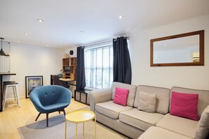 A modern living room with a sofa, a blue chair, a small table, and a window with curtains. - Meet Me in Willesden Green (London)