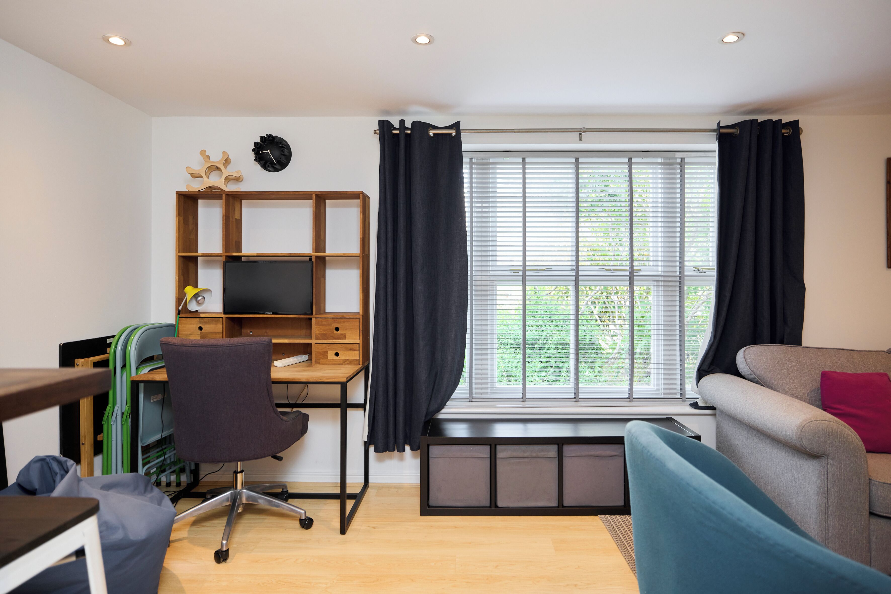 Un salon moderne avec un bureau en bois, un canapé confortable et une fenêtre équipée de stores.