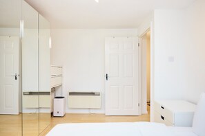 A minimalist room with a bed, a radiator, a white wardrobe, and a door. - Meet Me in Willesden Green (London)