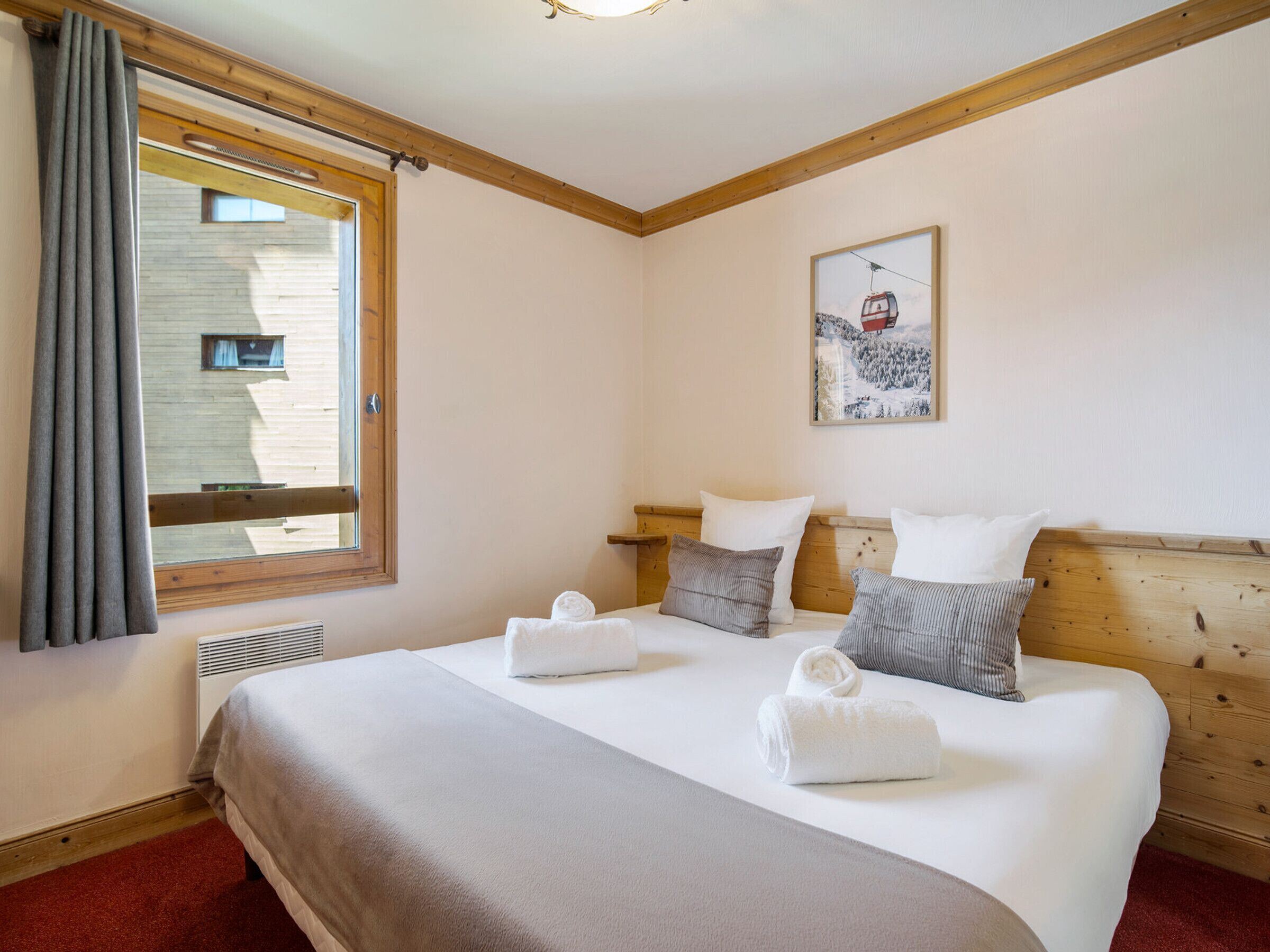 A hotel room with a large bed, a window with curtains, a painting on the wall, and a wooden headboard.