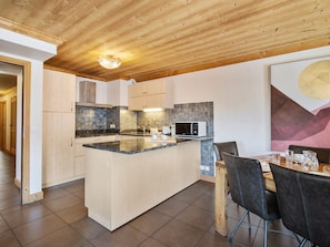 A modern kitchen with a central island, wooden ceiling, and a dining area with a table and chairs. - Spacious central apartment - 10 guests (Val Thorens)