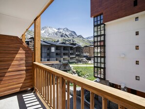 A wooden balcony with a view of a mountain range and a hotel building. - Spacious central apartment - 10 guests (Val Thorens)
