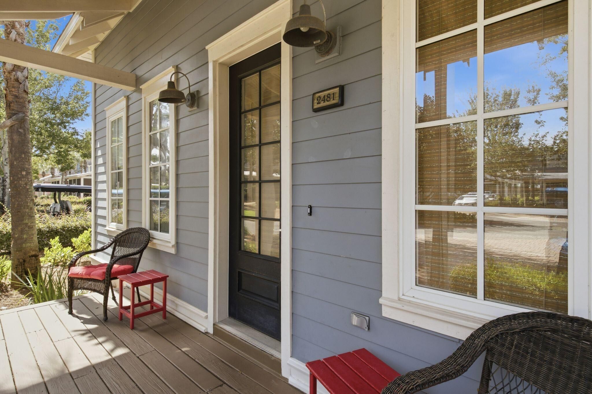 A porch with two wicker chairs, a small red table, and a black door with a number plate.
