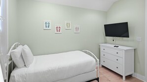 Quarto com uma cama de solteiro, cômoda e televisão de tela plana na parede.