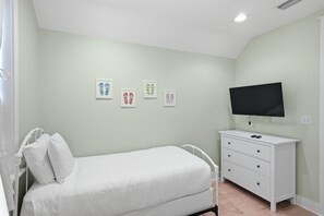 Een slaapkamer met een enkel bed, een dressoir en een flatscreen televisie aan de muur.