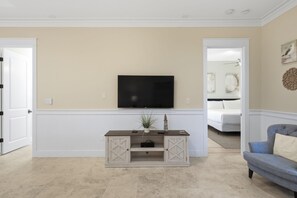 Een woonkamer met een flatscreen televisie aan de muur, een houten dressoir met lades, een blauwe bank en een bed op de achtergrond.