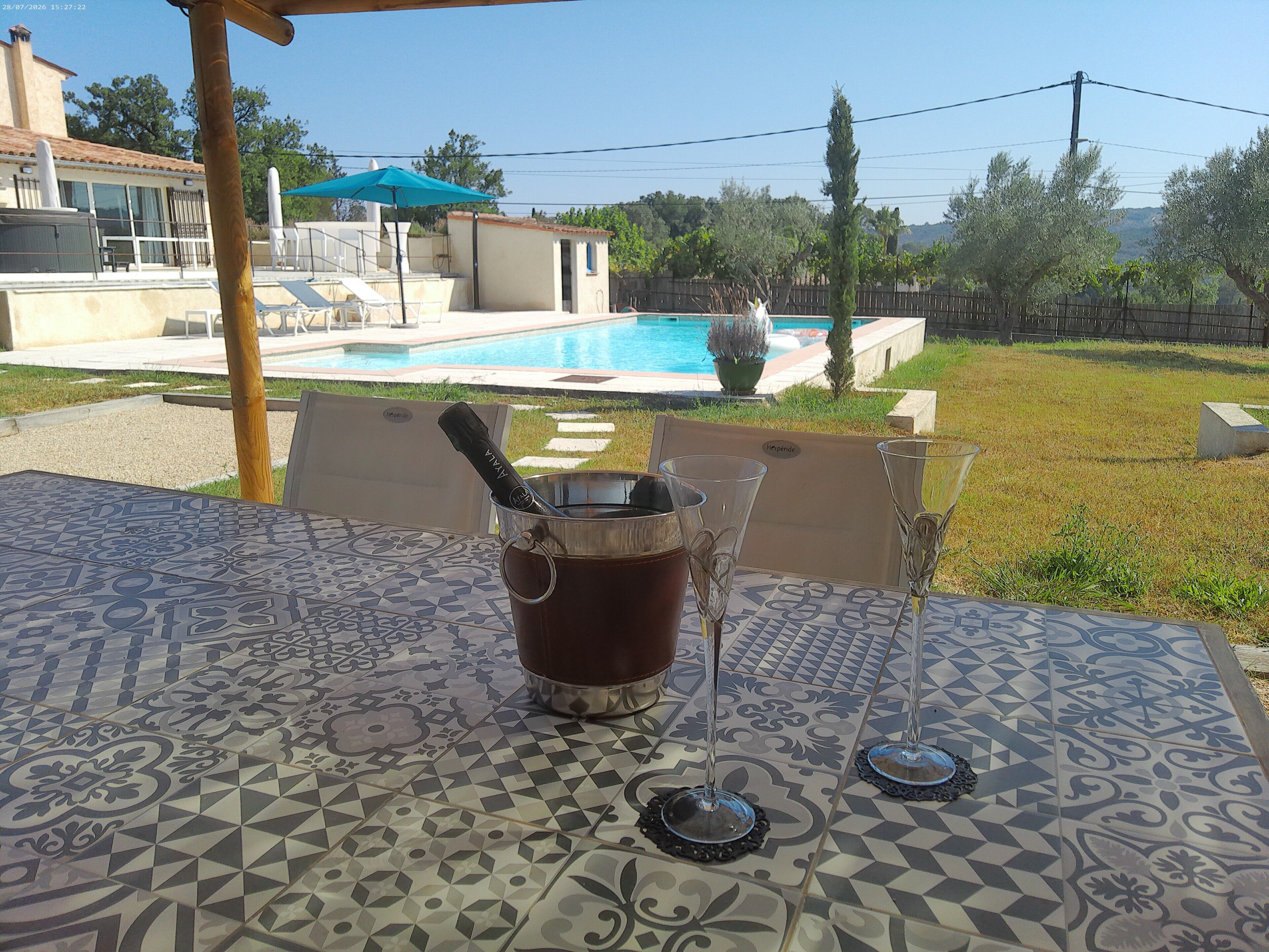 A patio area with a table, a drink, and a view of a swimming pool.