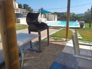 Una parrilla, una mesa y una piscina en un patio trasero.
