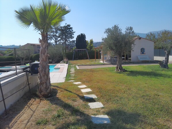 Un espacio exterior residencial con piscina, una palmera, un sendero de piedra y un edificio con un banco.