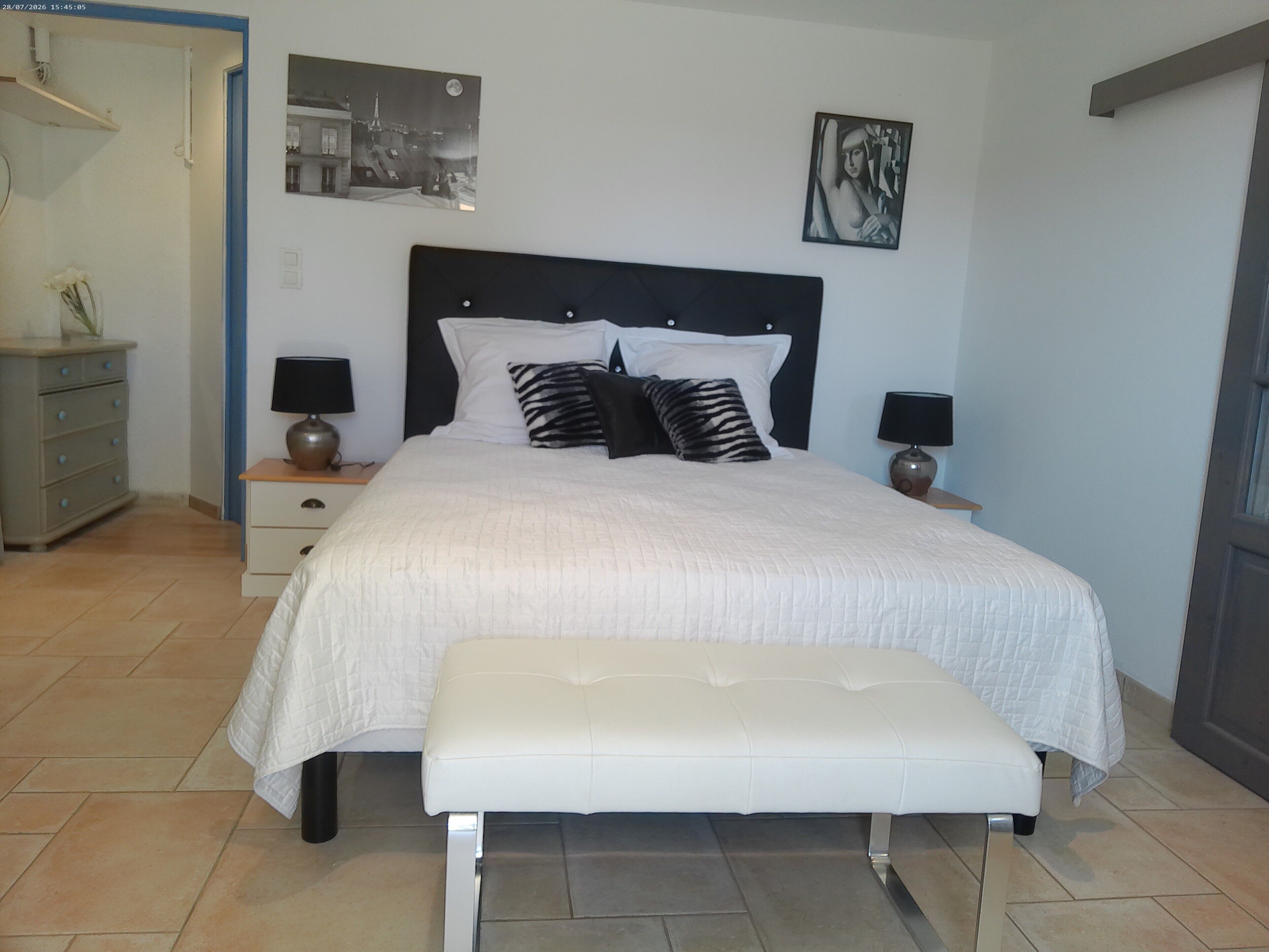 A neatly made bed with a headboard, two bedside lamps, and a bench in front.