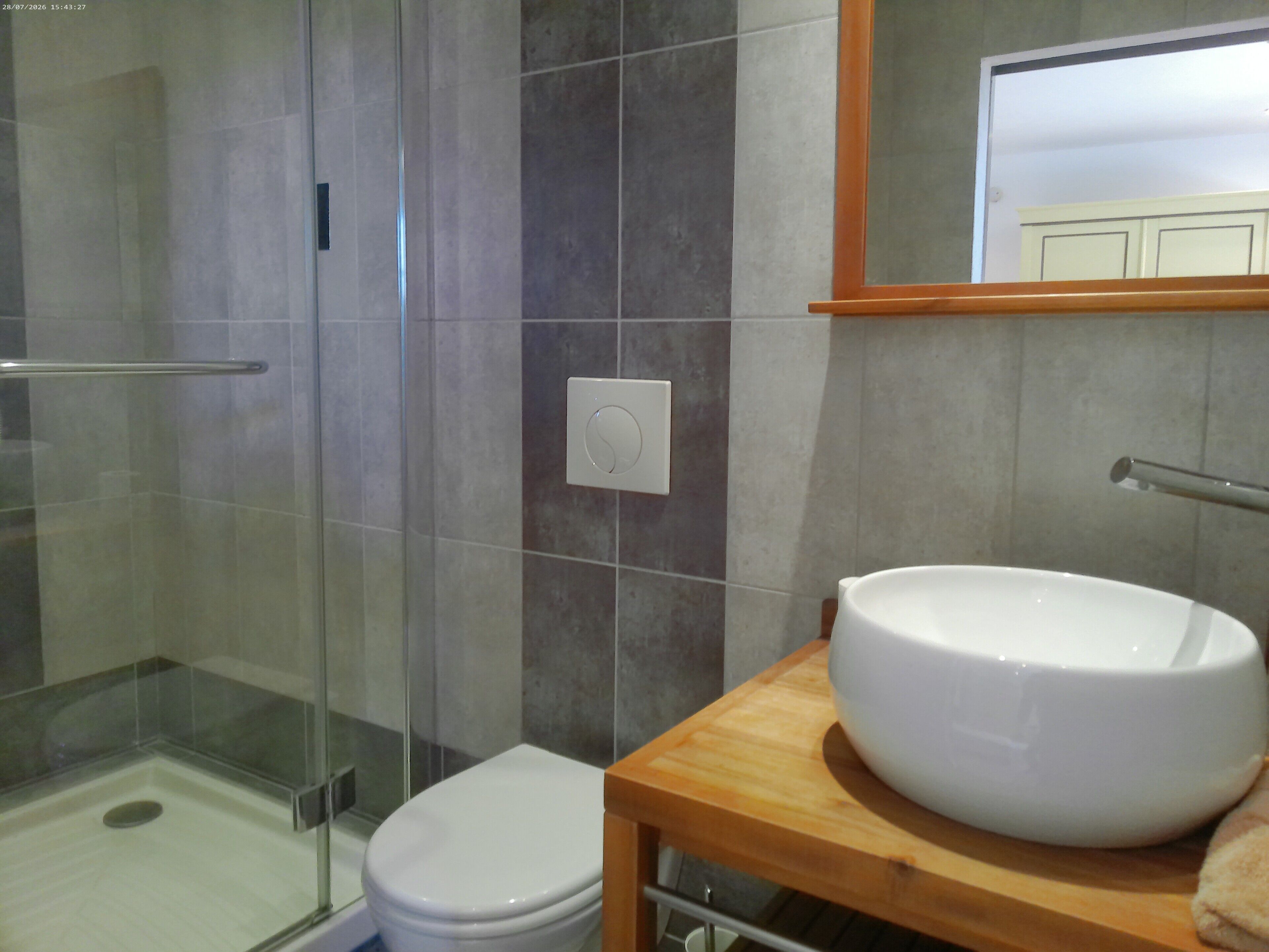 A bathroom with a glass shower enclosure, a white toilet, and a wooden vanity with a large white sink.
