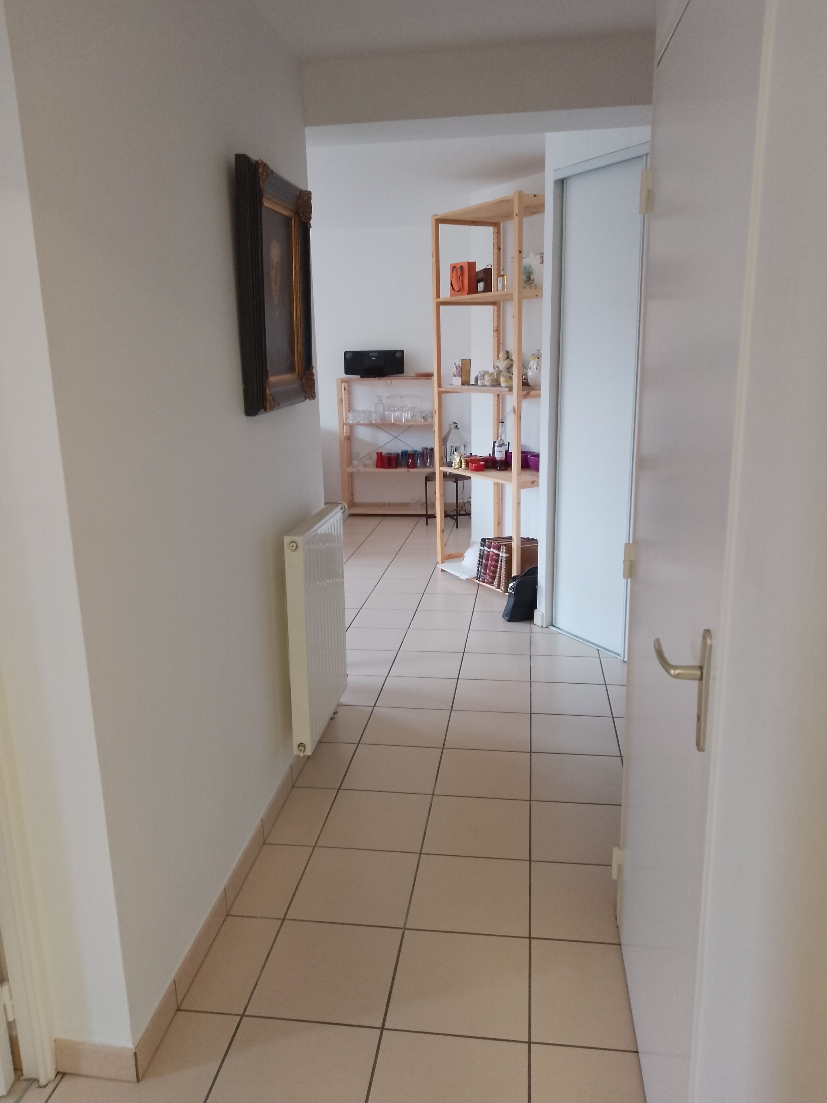 Un pasillo con un radiador, una estantería de madera y una puerta con manija.