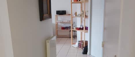 Un couloir avec un radiateur, une étagère en bois et une porte dotée d’une poignée.