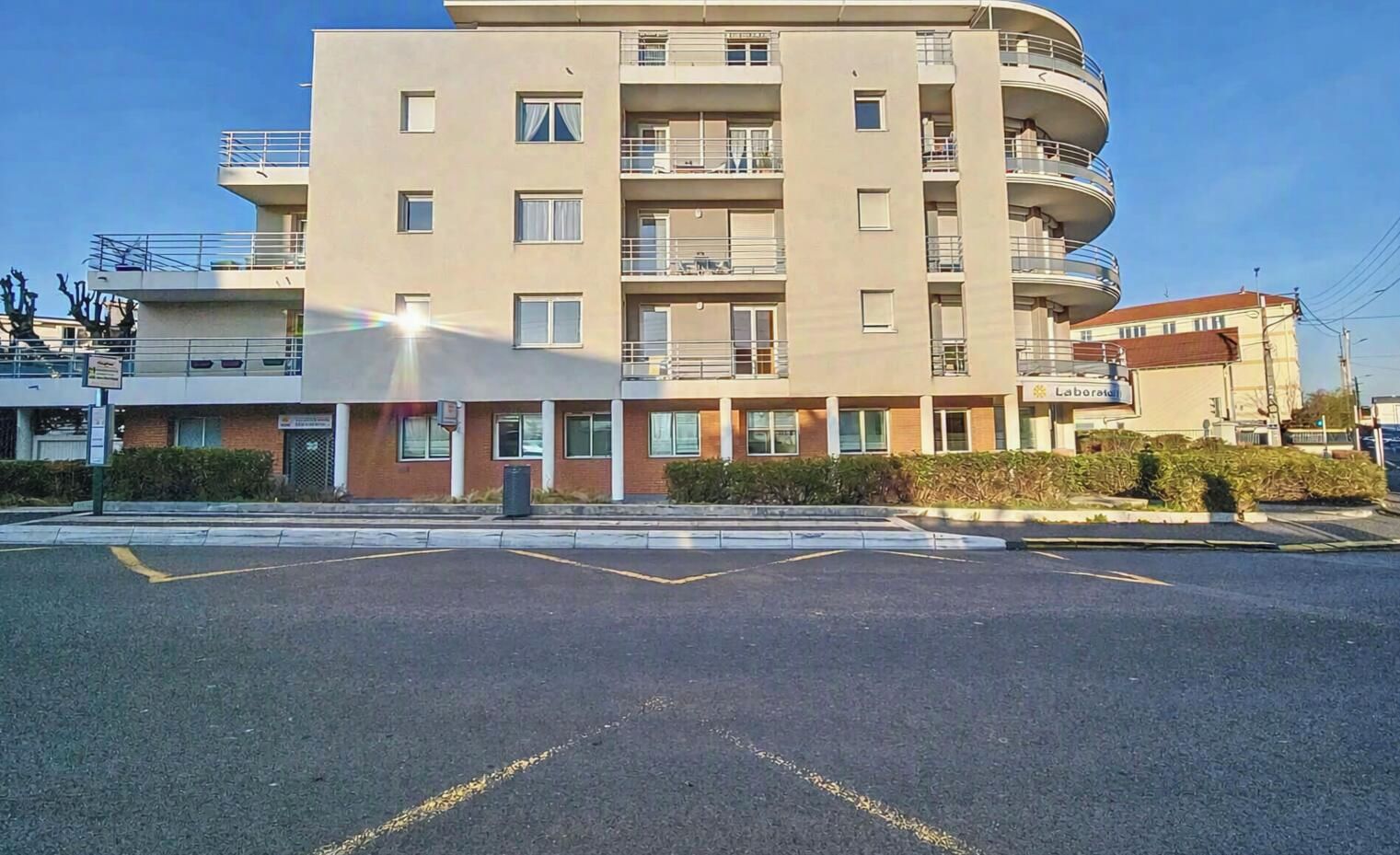 A multi-story building with a flat facade, multiple balconies, and a parking lot in front.