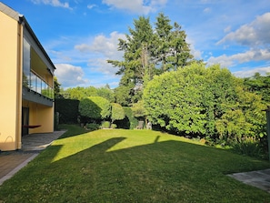 Ein gepflegter Garten mit Rasen, verschiedenen Bäumen und einem Gebäude mit Balkon.