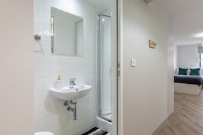 Ein modernes Badezimmer mit einem weißen Waschbecken, einer Duschkabine aus Glas und einer sichtbaren Toilette.