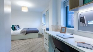 A modern bedroom with a bed, a desk, a chair, a window, and a wall-mounted shelf. - Student Only The Fitzalan (Cardiff)