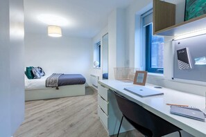 Ein modernes Schlafzimmer mit einem Bett, einem Schreibtisch, einem Stuhl, einem Fenster und einem Wandregal.