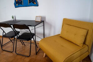 Ein Zimmer mit einem gelben Sofa, einem kleinen Tisch mit Stühlen, einer Zimmerpflanze und einer gerahmten Speisekarte auf dem Tisch.