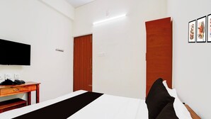 A hotel room with a bed, a desk with a telephone, a television mounted on the wall, and a door.