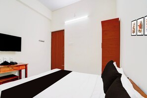 Una habitación de hotel con una cama, un escritorio con teléfono, un televisor fijado a la pared y una puerta.