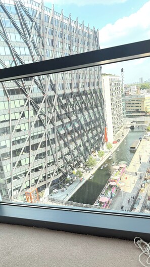 Ein modernes Gebäude mit einem markanten, winkelförmigen Design, ein Fluss mit Booten und ein Fußgängerweg.