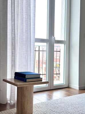 Ein Zimmer mit Holztisch, Fenster mit Blick auf Gebäude und einem weißen Vorhang.