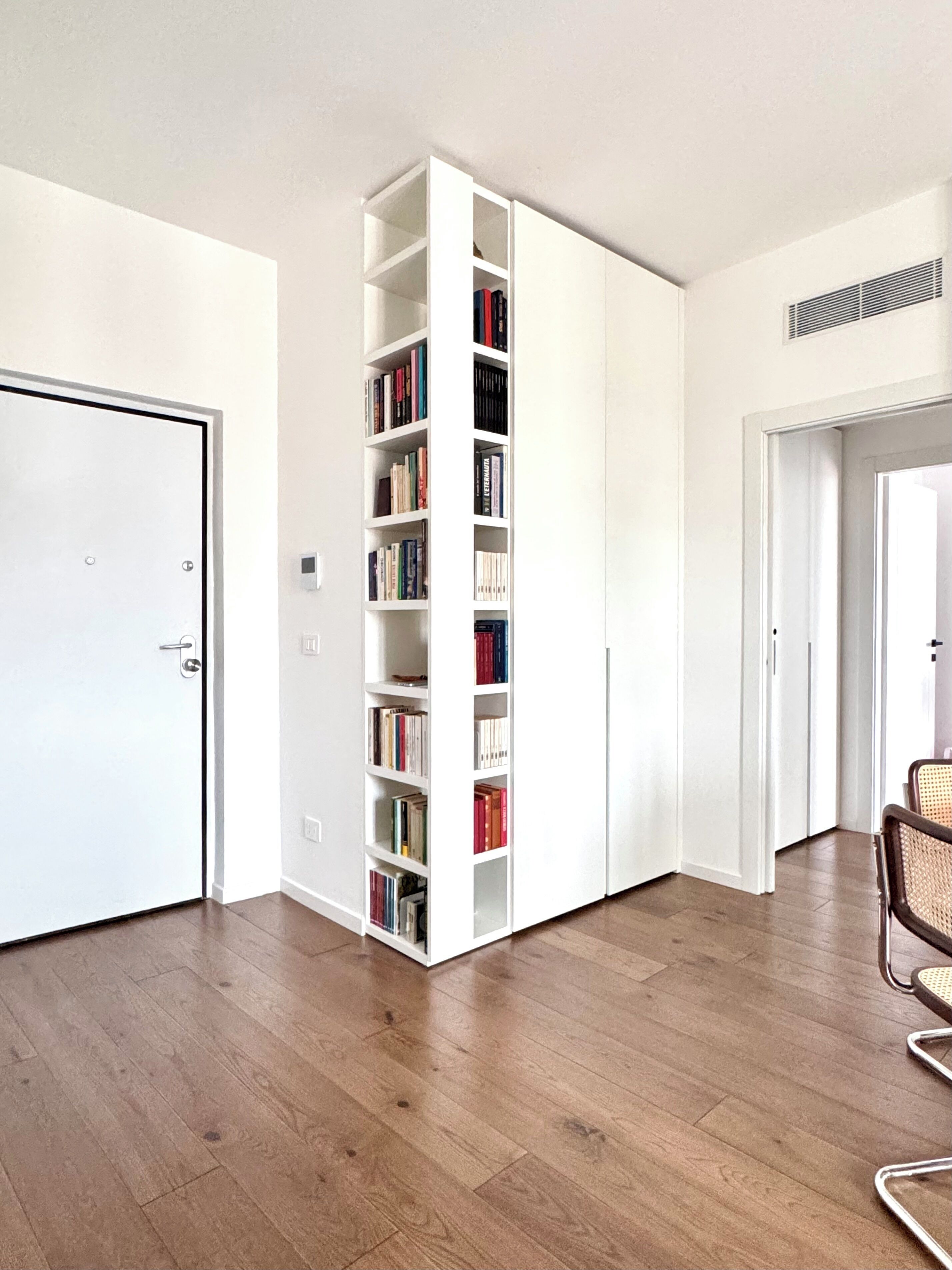 A room with a white bookshelf, wooden flooring, and a door.