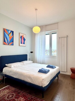 A bedroom with a bed, two paintings, a window, a radiator, and a hanging light fixture. - Skyline Design Apartment - Top Floor Next to the Metro (Milano)
