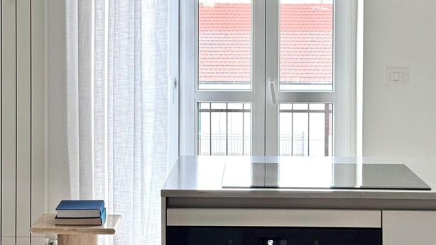 Een moderne keuken met een ingebouwde oven, een raam met uitzicht op een gebouw met rode daken, en een hanglamp.