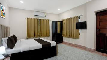 Une chambre d’hôtel avec un lit, des rideaux, un appareil de climatisation, une télévision et une porte.