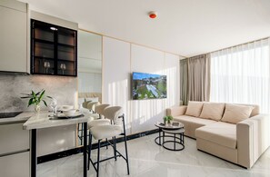 Ein modernes Wohnzimmer mit einer Couch, einem Essbereich mit Stühlen, einem kleinen runden Tisch und einem Fernseher, der eine Landschaft zeigt.