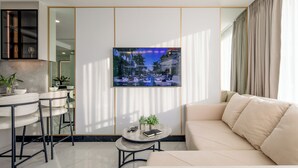 Un salon moderne comprenant un canapé, une table basse, un téléviseur fixé au mur et un coin cuisine avec des tabourets de bar.