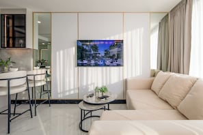 A modern living room with a sofa, a coffee table, a TV mounted on the wall, and a kitchen area with bar stools.