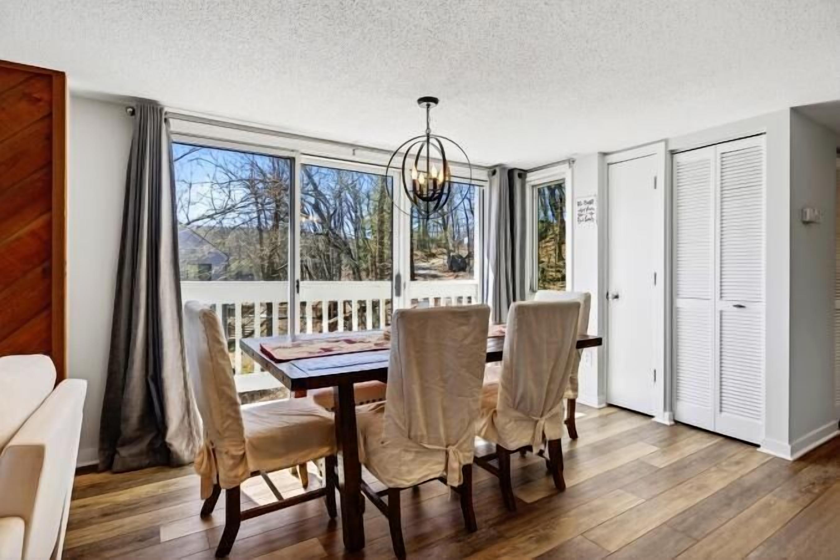 A dining area with a table and chairs, a view through a glass door, and a wooden floor.