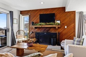 Un salón acogedor con chimenea, un televisor montado en una pared de madera y una zona de estar cómoda.
