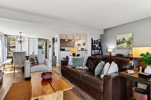 A modern living room with a sofa, armchair, and coffee table. There is a kitchen area in the background. - Ledges 50 with Wintergreen Advantage (Wintergreen)