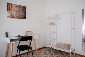Una habitación con un escritorio blanco, una silla negra, un armario blanco, un cuadro enmarcado y una planta en maceta.