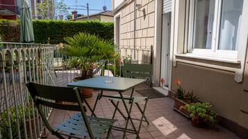 Una terrazza esterna con tavolo e sedie, circondata da piante in vaso e una recinzione metallica.