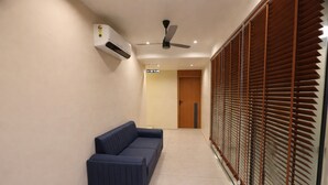 A hallway with a blue sofa, an air conditioning unit, a ceiling fan, and a door leading to another room. - Hotel Rio Valley (Rajkot)