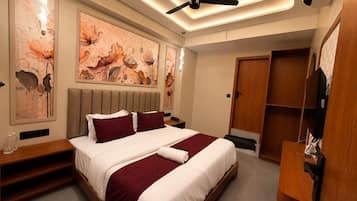 A modern hotel room with a bed, artwork on the walls, a ceiling fan, and a wooden wardrobe.