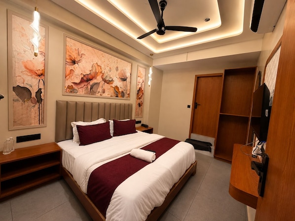 A modern hotel room with a bed, artwork on the walls, a ceiling fan, and a wooden wardrobe. - Hotel Rio Valley (Rajkot)