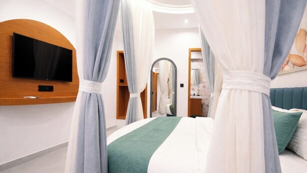 A bedroom with a bed, curtains, a TV mounted on the wall, and a mirror. - Hotel Rio Valley (Rajkot)