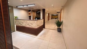 A hotel reception area with a marble counter, a potted plant, and a tiled floor. - Hotel Rio Valley (Rajkot)