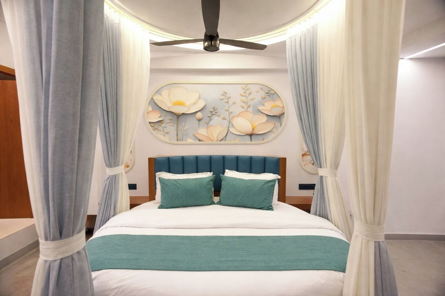 A bed with a canopy, a ceiling fan, and a wall with floral artwork.