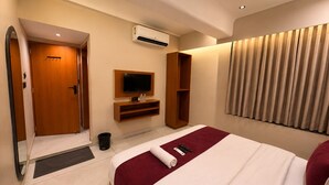 A hotel room with a bed, a television, an air conditioning unit, a wooden wardrobe, a mirror, and a window with curtains. - Hotel Rio Valley (Rajkot)