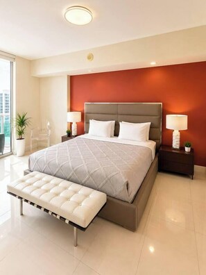 Ein modernes Schlafzimmer mit einem großen Bett, Nachttischen, einer Bank und Blick auf die Stadt.