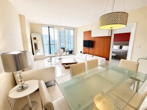 A modern living room with a glass dining table, white sofas, and a large window with a city view. - Incredible 1 Bedroom Apt 43rd Floor at Icon Brickell (Miami)