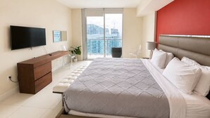 A modern bedroom with a bed, a TV, a dresser, and a balcony with a view of buildings. - Incredible 1 Bedroom Apt 43rd Floor at Icon Brickell (Miami)