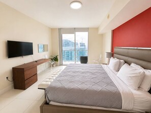 A modern bedroom with a bed, a TV, a dresser, and a balcony with a view of buildings. - Incredible 1 Bedroom Apt 43rd Floor at Icon Brickell (Miami)